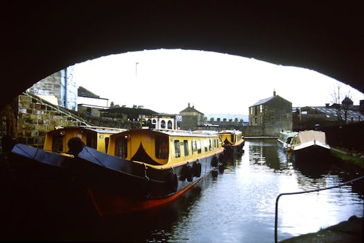 Charming narrowboats on Leeds and Liverpool Canal under bridge in Skipton, UK, showcasing serene waterside life.