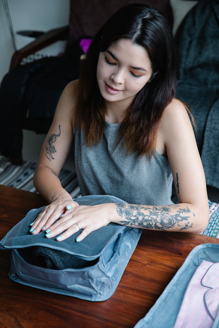 Asian woman with tattoos organizing clothes in a travel bag indoors.