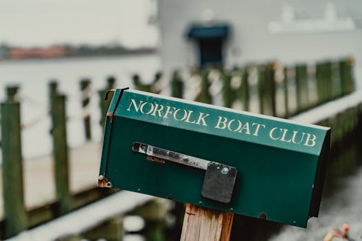 Dark green letter box with inscription Norfolk Boat Club located near wooden fence in winter countryside